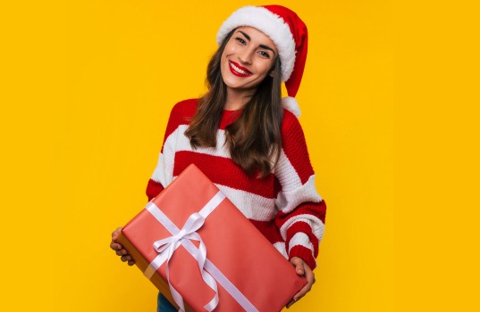 Frau mit Weihnachtsmann-Mütze hält Weihnachtsgeschenk und lächelt